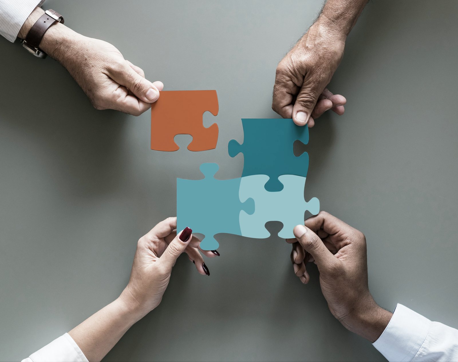 Four hands fitting puzzle pieces together
