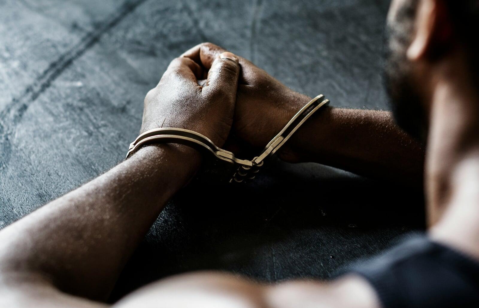 Hands in handcuffs resting on a dark surface